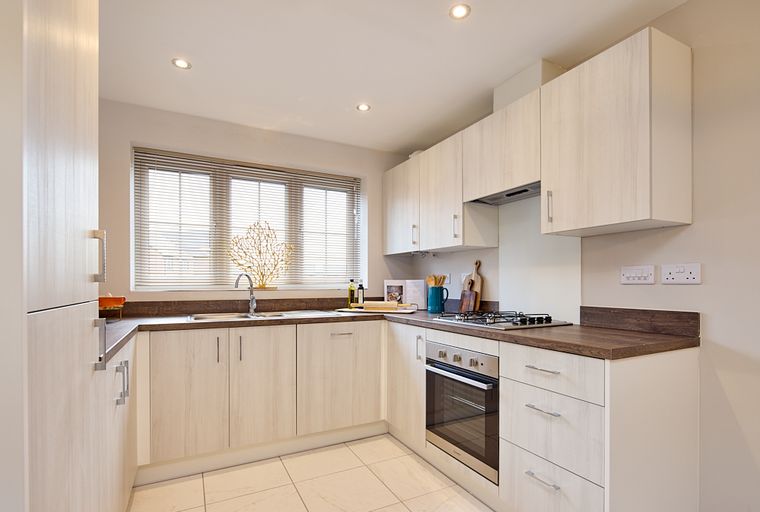 A modern L-shaped kitchen with light wood cabinets, a sink, a window, and appliances.