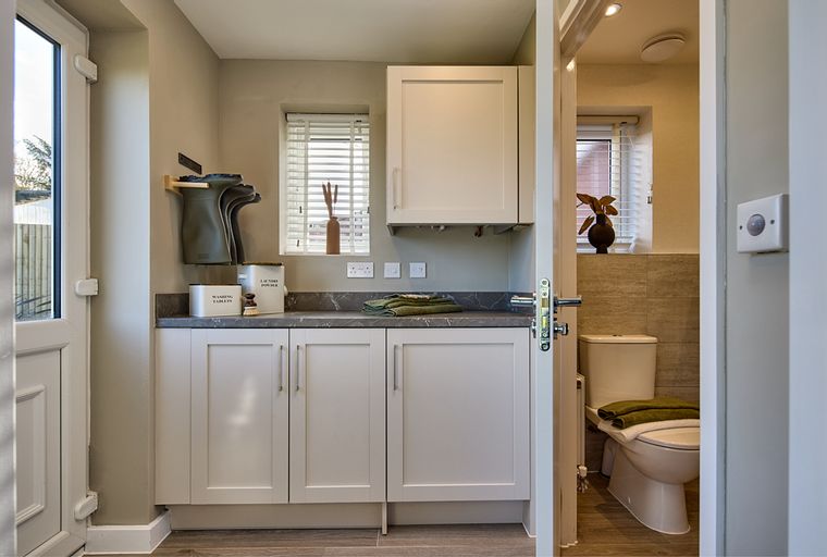 A laundry room with white cabinets and a countertop, featuring a door to a small bathroom with a toilet.
