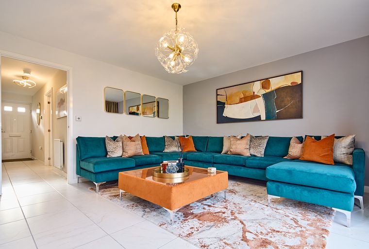 A living room with a teal sectional sofa, an orange ottoman coffee table, and abstract art.