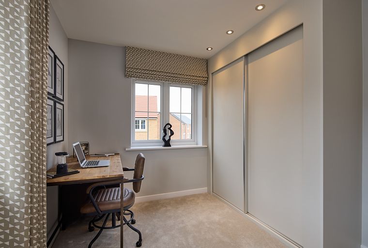 A bedroom with a desk, chair, laptop, window, and a large wardrobe.