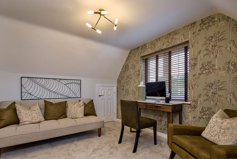 A home office with a sofa, desk, computer, and patterned wallpaper.