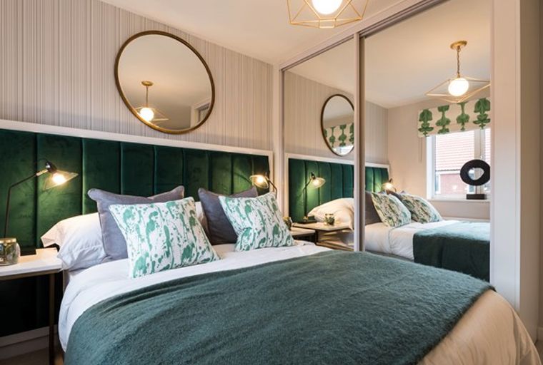 A bedroom with a bed, headboard, bedside tables, lamps, and a mirror.