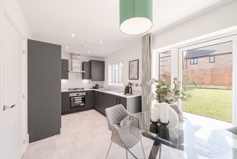 A modern kitchen and dining area with dark grey cabinets, a glass dining table, and sliding doors leading to a backyard.
