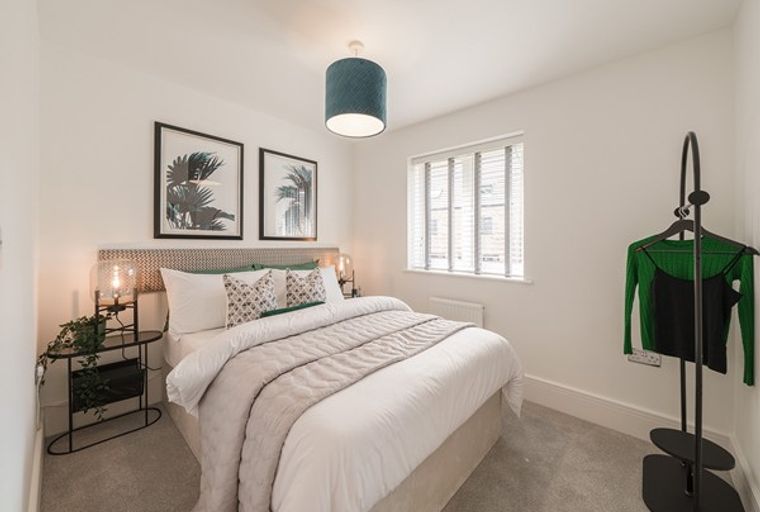 A bedroom with a bed, bedside tables, artwork, a window, and a clothing rack.