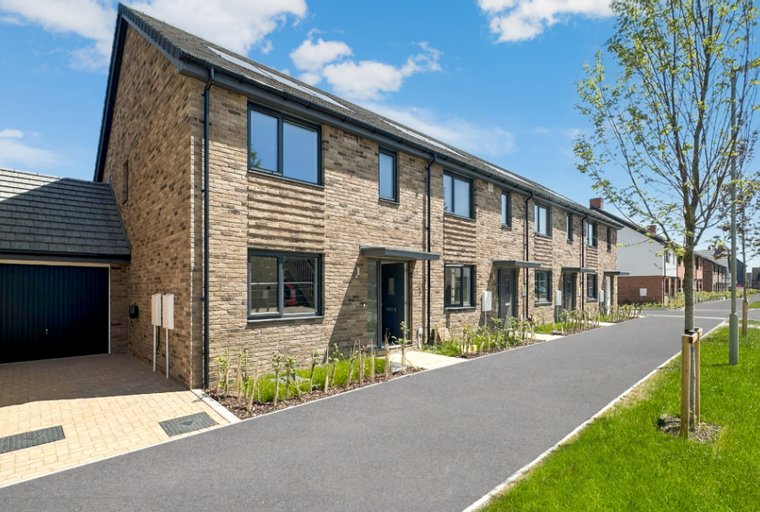 A row of modern townhouses with garages and paved driveways on a sunny day.