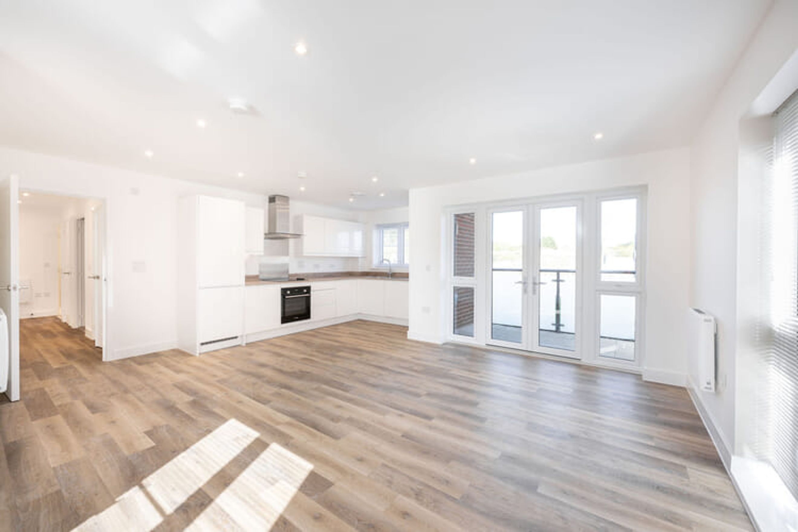 A modern open-plan living space with a kitchen and double doors leading to a balcony.