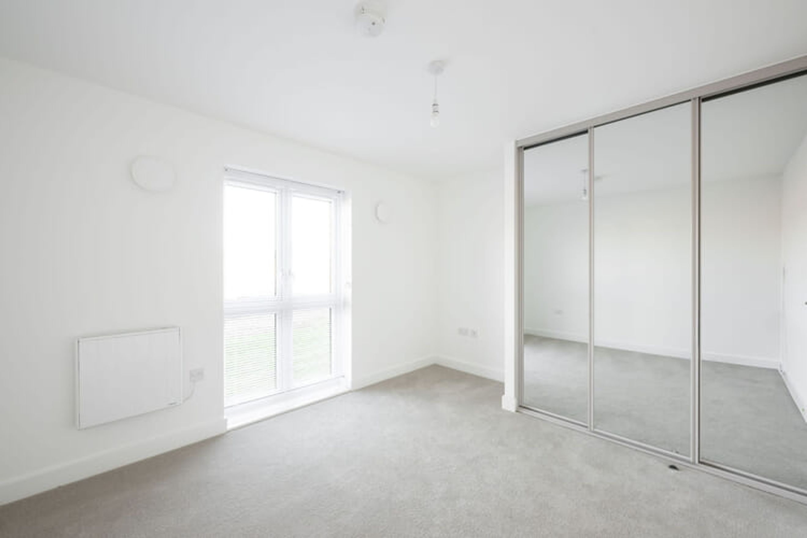 A bedroom with a large window, a mirrored wardrobe, and a heater.