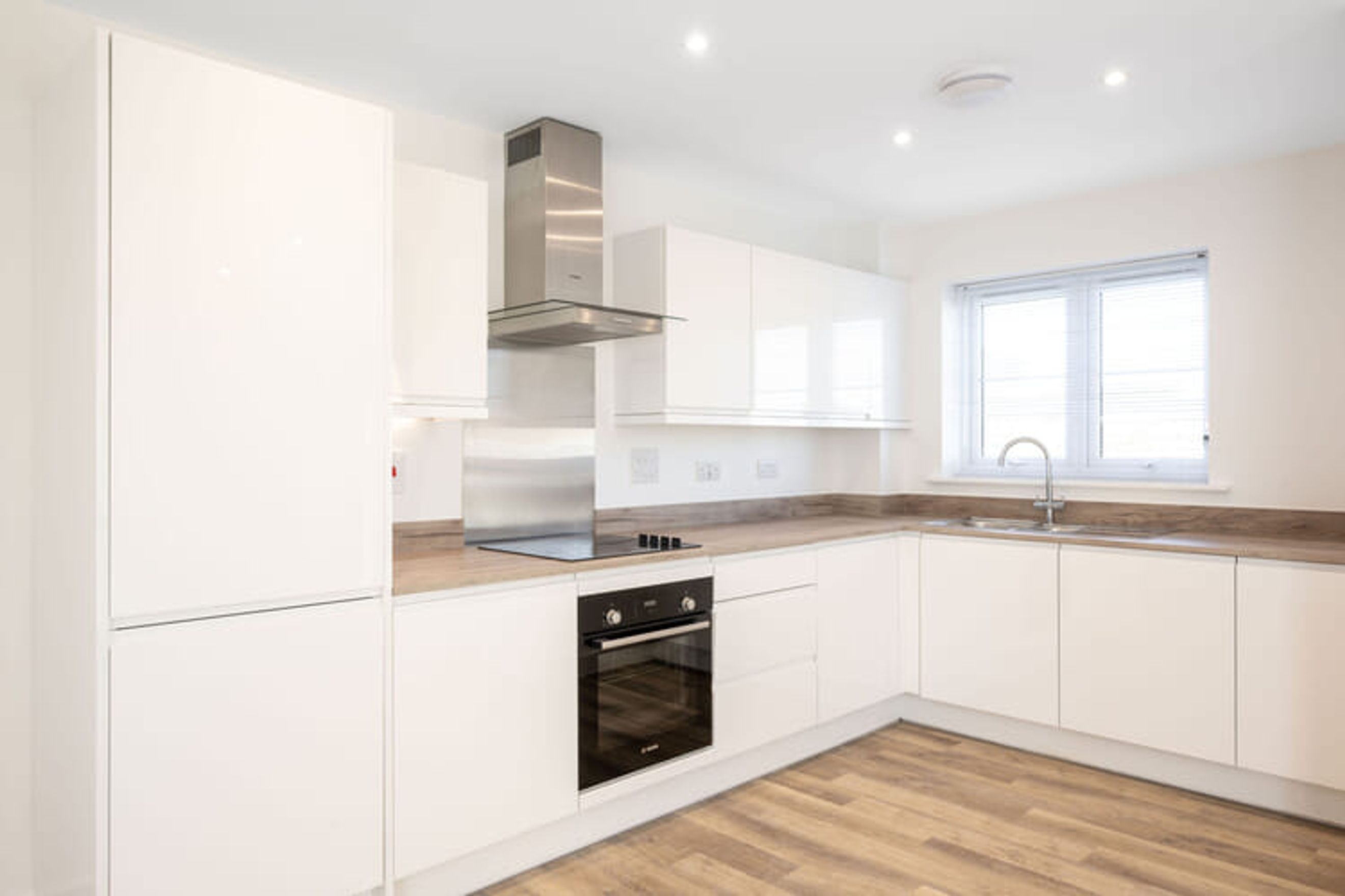 A modern kitchen with white cabinets, a stainless steel range hood, an oven, and a sink.