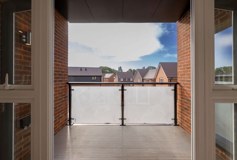 A balcony with a glass balustrade overlooking houses.