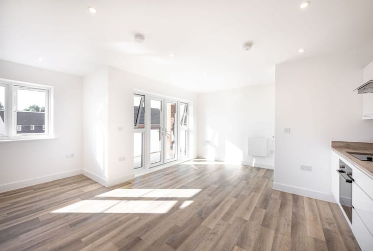 A spacious, empty living room and kitchen area with large windows and double doors.