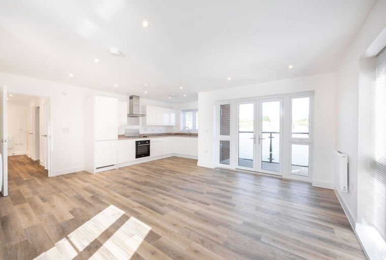 A modern open-plan living space with a kitchen and double doors leading to a balcony.
