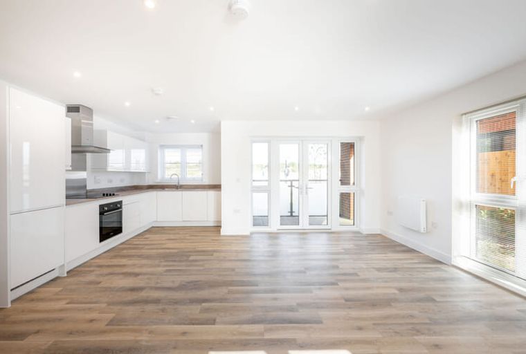 A modern kitchen and living area with white cabinets, an oven, a sink, and large glass doors leading to a balcony.
