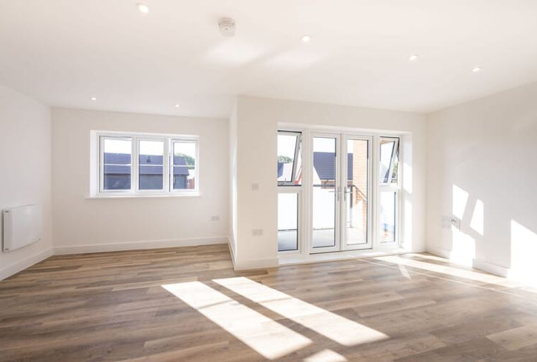 A living room with wood flooring, a window, and double doors.
