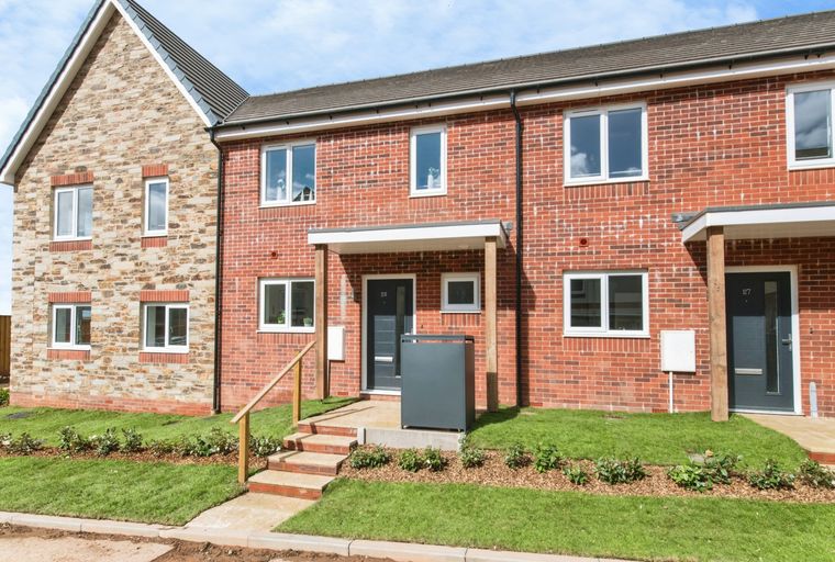 A row of modern townhouses with brick and stone facades, featuring multiple windows and front doors.