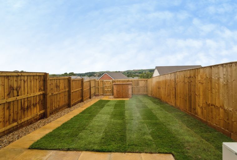 A backyard with a freshly mown lawn, wooden fences, a stone patio, and a wooden shed.