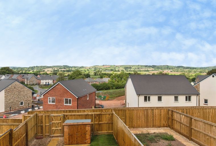 A backyard with a wooden fence, a shed, and a view of houses and rolling hills.