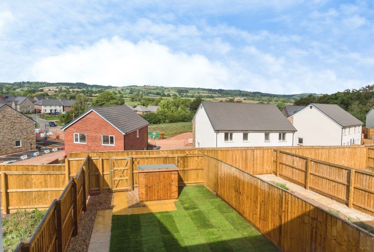 A backyard with a lawn, a wooden fence, a storage shed, and a gate.