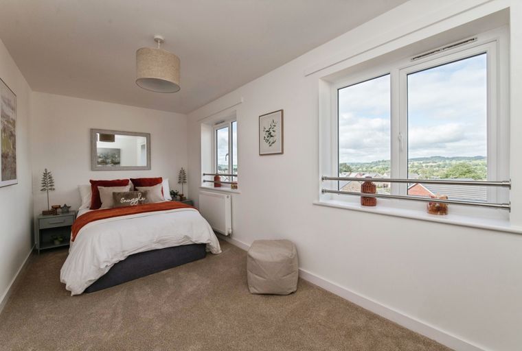 A bedroom with a bed, pillows, a bedside table, and a window.