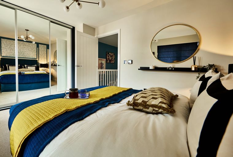 A bedroom with a bed, mirrored wardrobe, and a round mirror.
