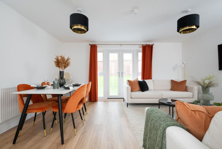 A dining area and living room with orange chairs, a white sofa, and French doors.