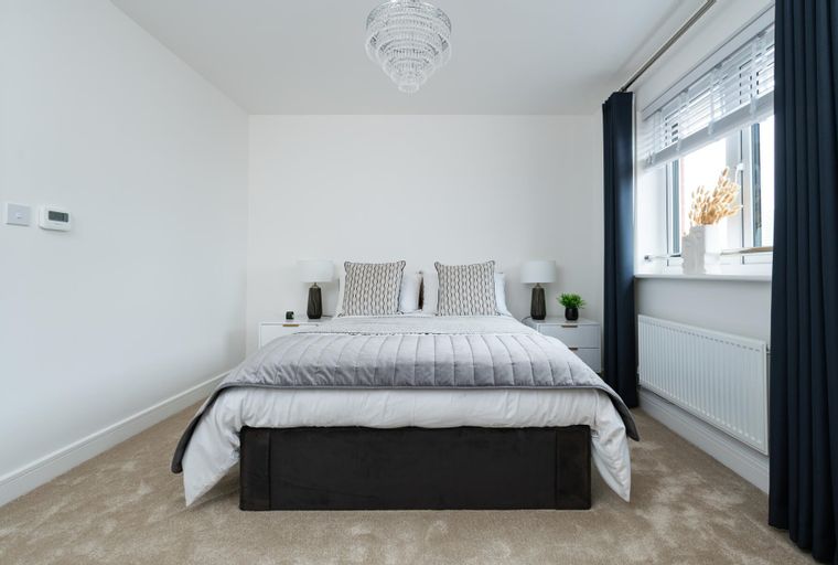 A bedroom with a bed, bedside tables, lamps, and a chandelier.
