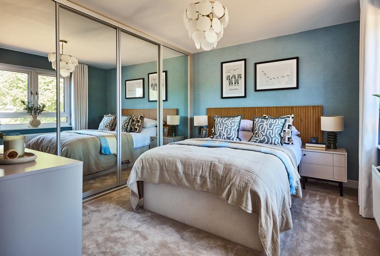 A bedroom with a bed, mirrored wardrobe, and bedside tables.