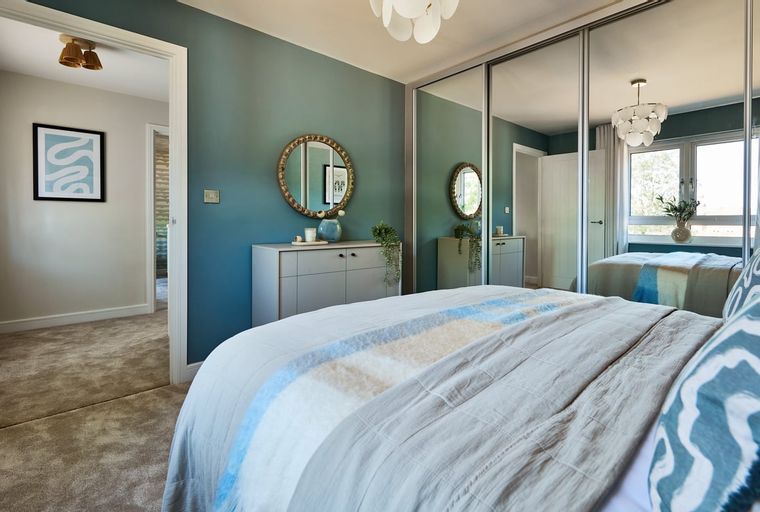 A bedroom with a bed, mirrored wardrobe, and dresser.