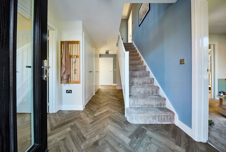 A hallway with a herringbone floor, a staircase, and a coat rack.
