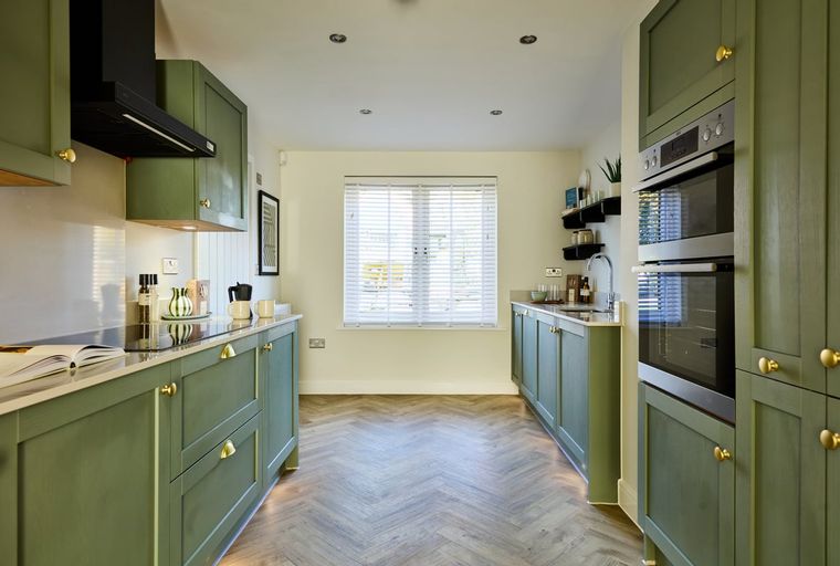 A modern kitchen with sage green cabinets, gold hardware, and a herringbone floor.
