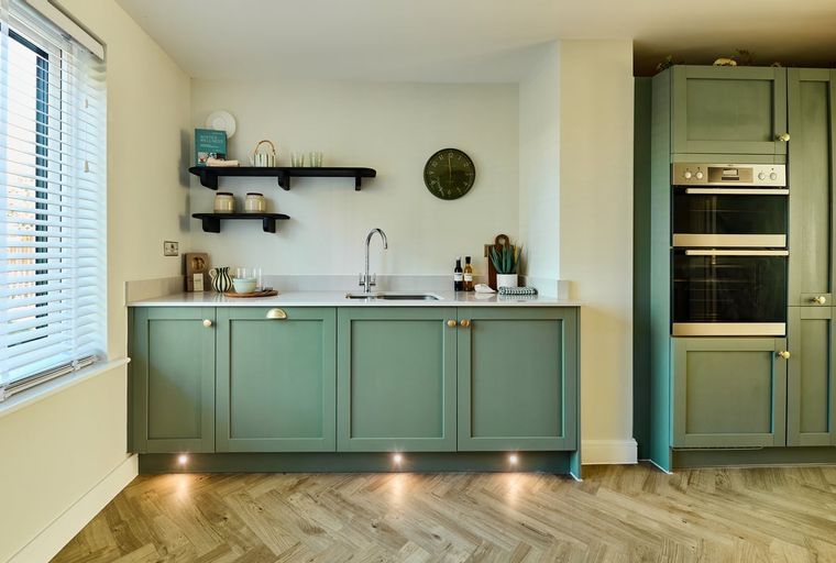 A kitchen with sage green cabinets, a sink, and a double oven.