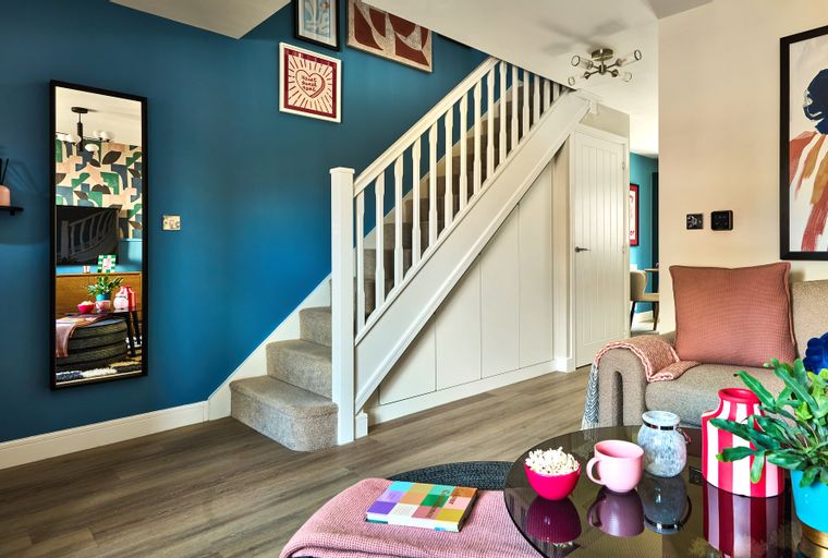 A hallway with a staircase, a mirror, and a living room area.