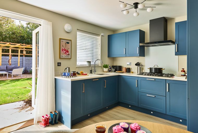 A kitchen with blue cabinets, a sink, a stove, and a doorway leading to a garden.