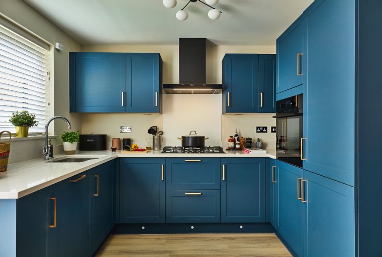 A modern kitchen with deep blue cabinets, white countertops, and gold hardware.