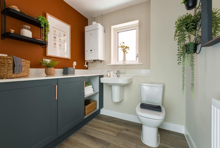 A laundry room with a sink, toilet, cabinets, and a wall-mounted boiler.
