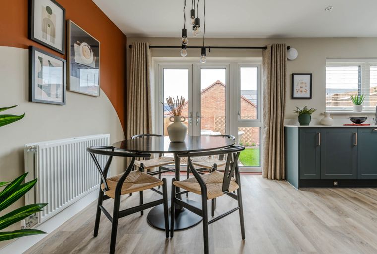 A dining area with a round table, chairs, and French doors leading to a garden.