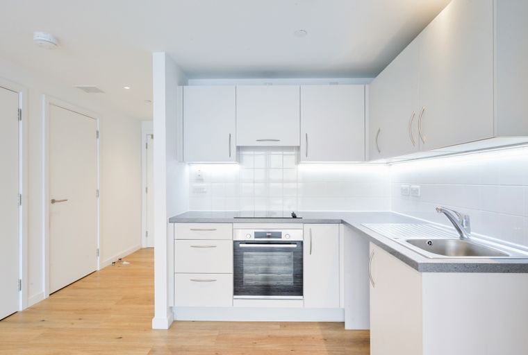 A modern kitchen with white cabinets, a grey countertop, an oven, and a sink.