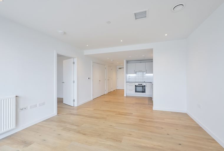 A spacious, empty room with a modern kitchen area and multiple doors.