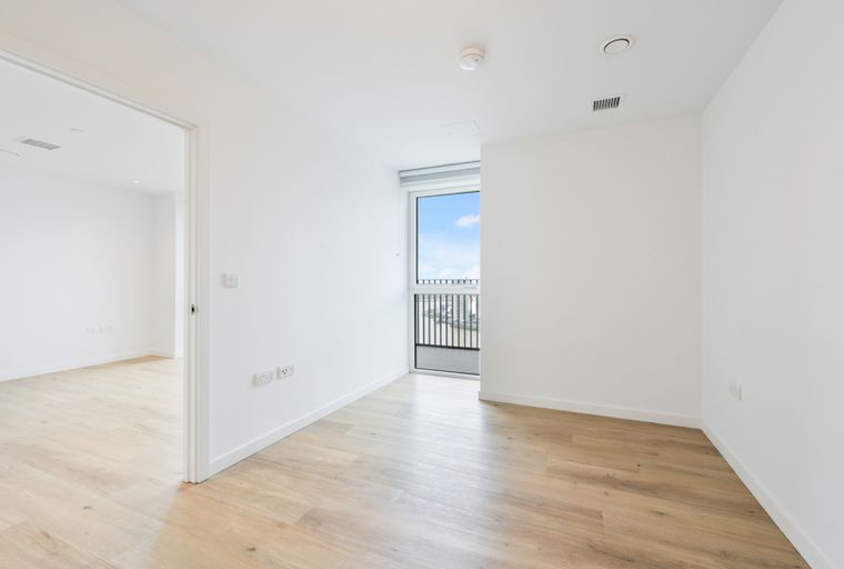 A view of an empty room with light wood floors and a large window.