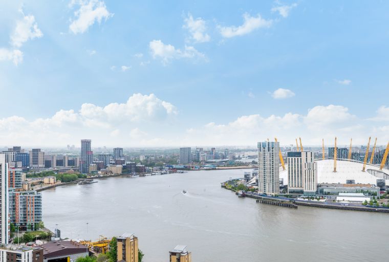 A cityscape with a river, modern buildings, and the O2 Arena under a cloudy sky.