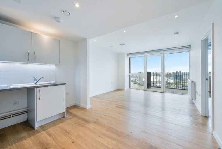 A modern apartment interior with a kitchen area and a living space with large windows overlooking a city view.