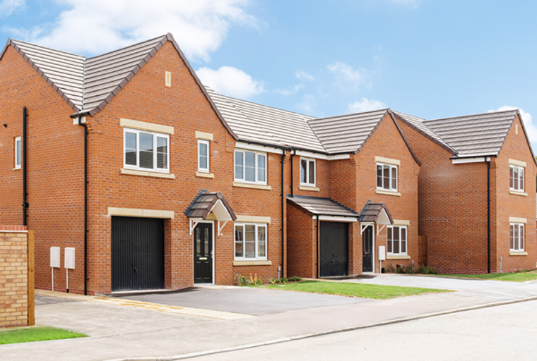 A row of modern brick townhouses with garages and front doors under a blue sky.