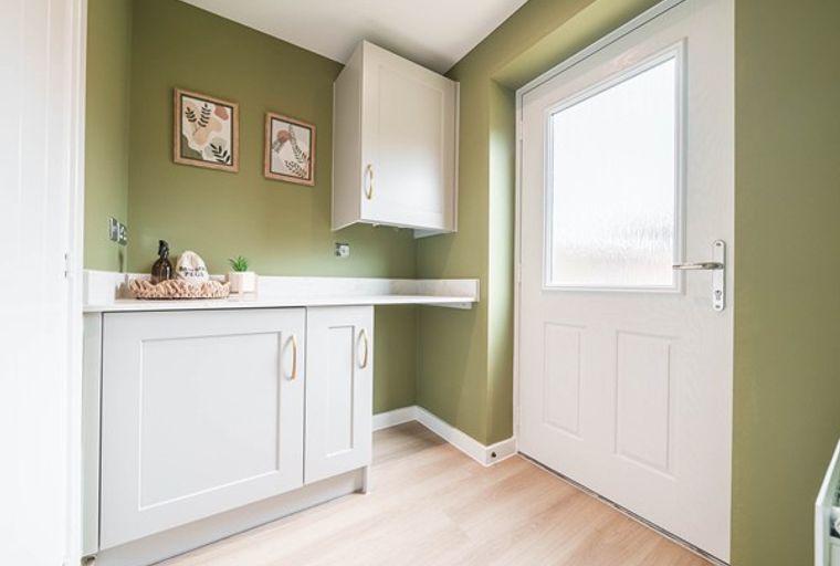 A laundry room with white cabinets, a white countertop, and a white door with a frosted glass window.