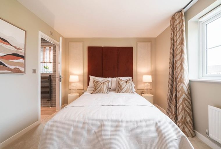 A bedroom with a bed, headboard, bedside lamps, and a window with curtains.