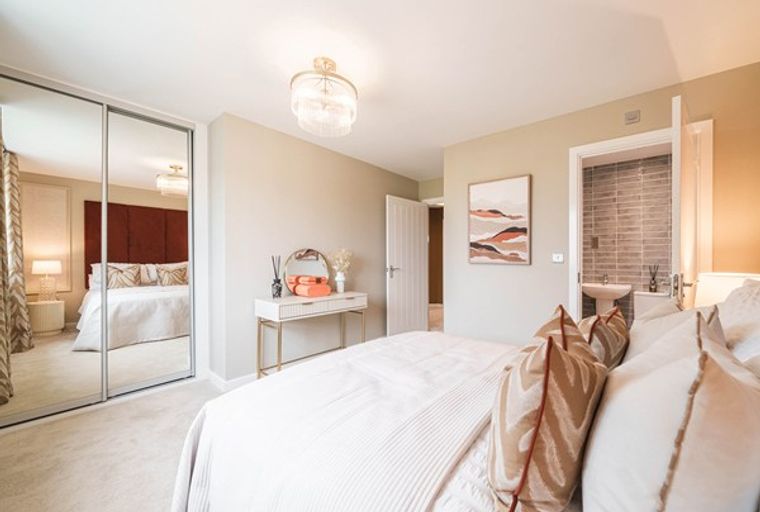 A bedroom with a bed, mirrored wardrobe, and a vanity table.