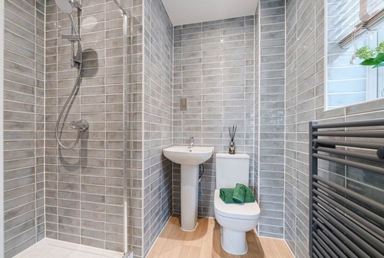 A bathroom with a shower, sink, toilet, and heated towel rail.