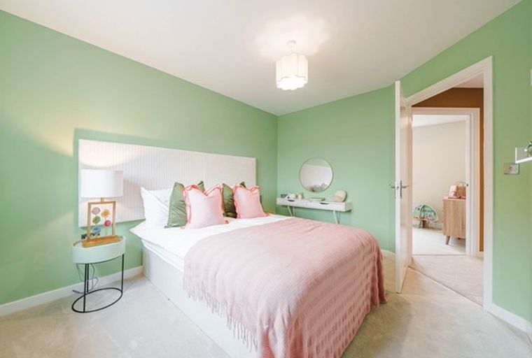A bedroom with a bed, pillows, a throw blanket, a bedside table with a lamp, and a vanity.