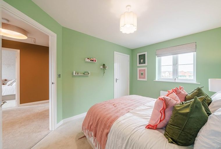 A bedroom with a bed, pillows, a throw blanket, shelves, framed art, a window, and a doorway.