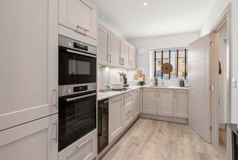 A modern kitchen with light-colored cabinets, integrated ovens, and a window.