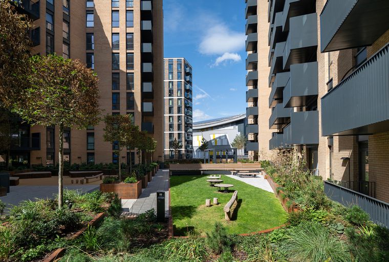 A courtyard with apartment buildings, a lawn, trees, and outdoor seating.