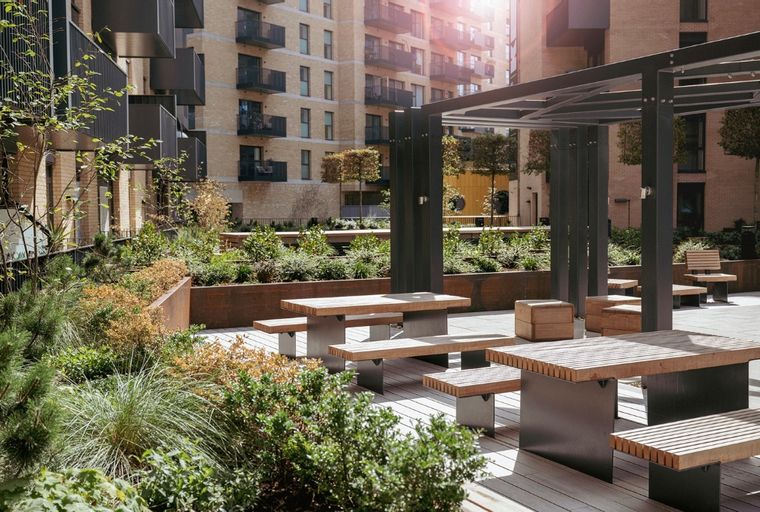 A courtyard with picnic tables and benches surrounded by greenery and modern buildings.